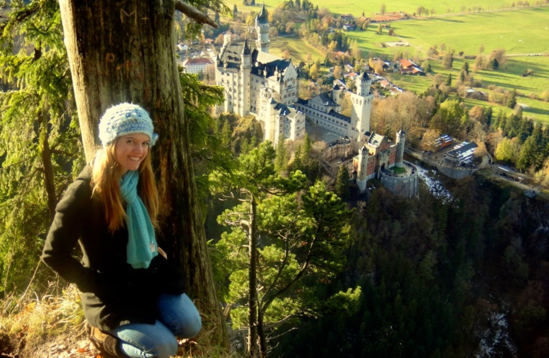 a woman smiling on a mountainside with a large castle below