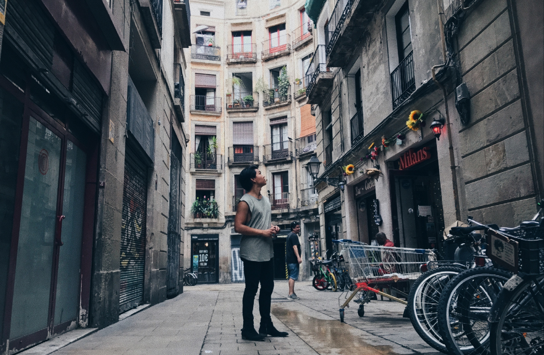 a man looking up while standing in the middle of a street lined with gothic style buildings with balconies