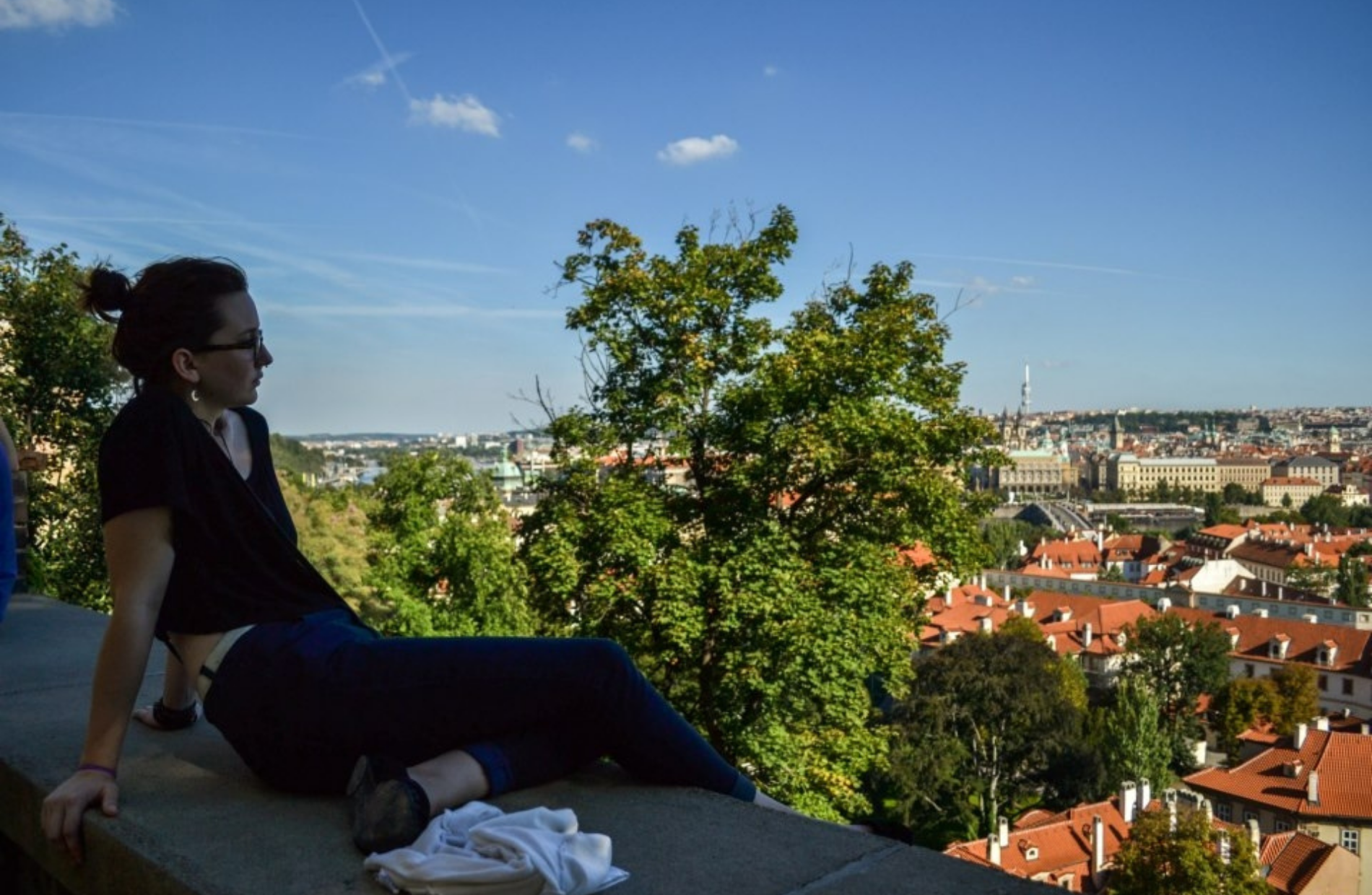 woman sitting along the edge of a stone ledge overlooking the red roof topped buildings below