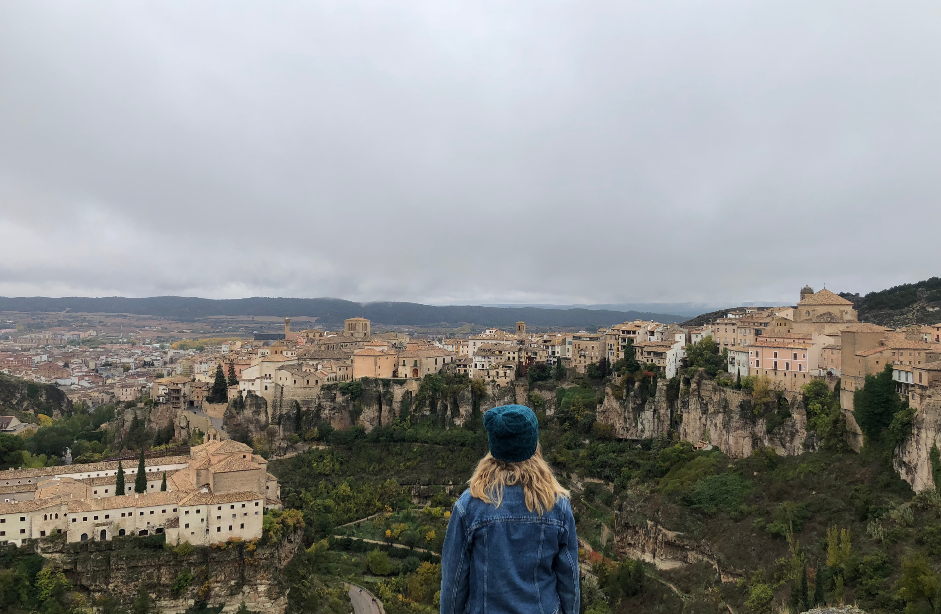 the back of a woman with a cap with a mountain range with medieval buildings in the background