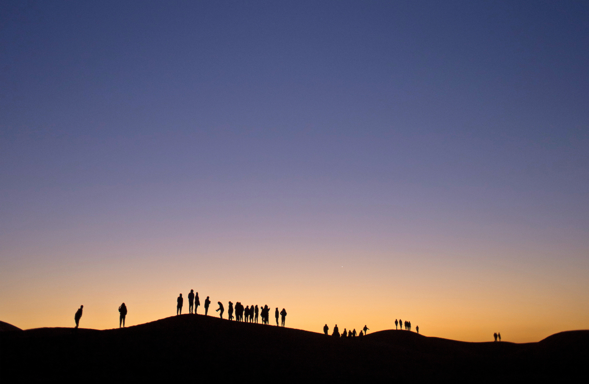 sunset view of row of people silhouette on sand dunes