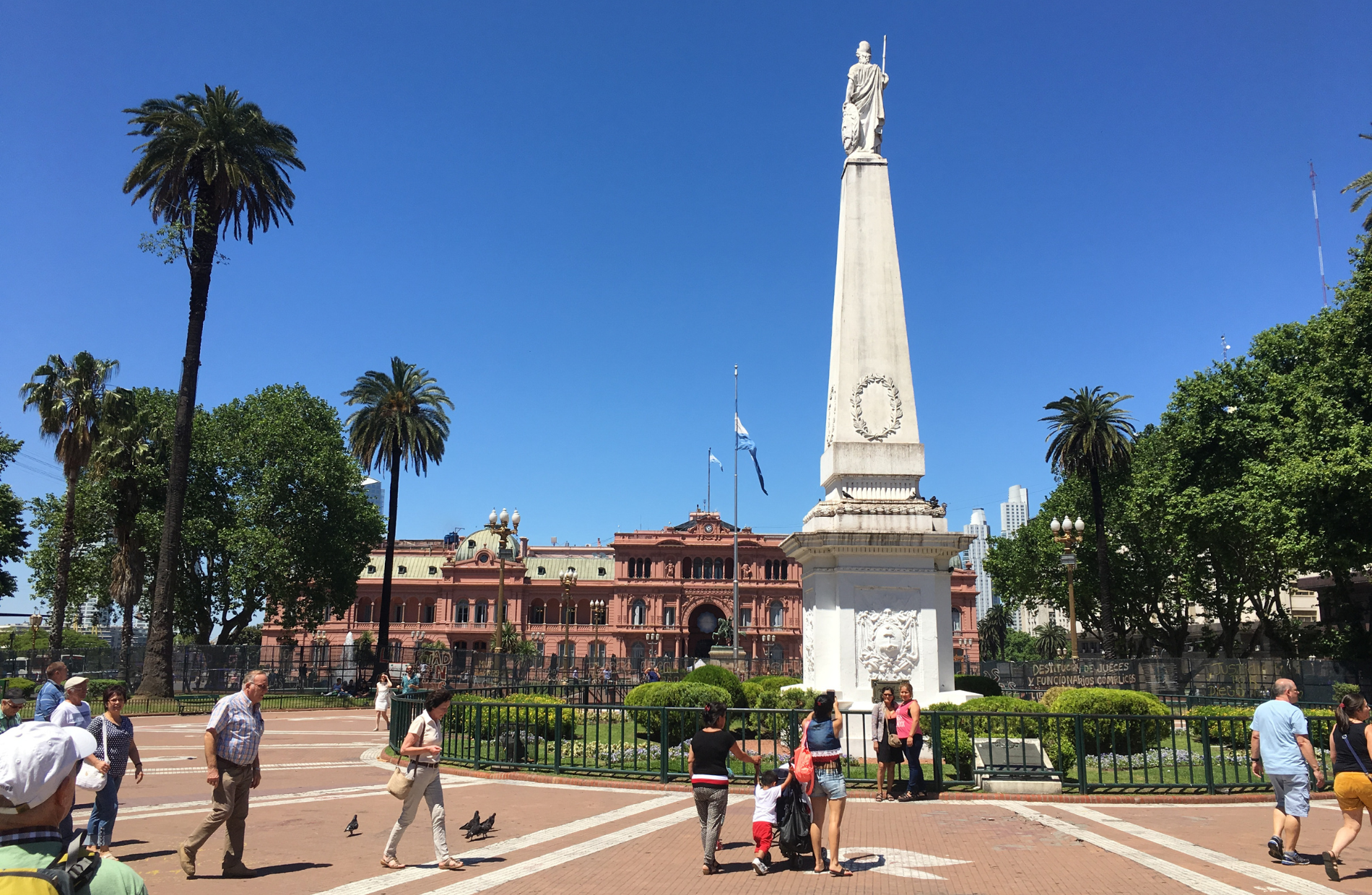 people taking photos in front of a tall monument with a statue on top of the obelisk