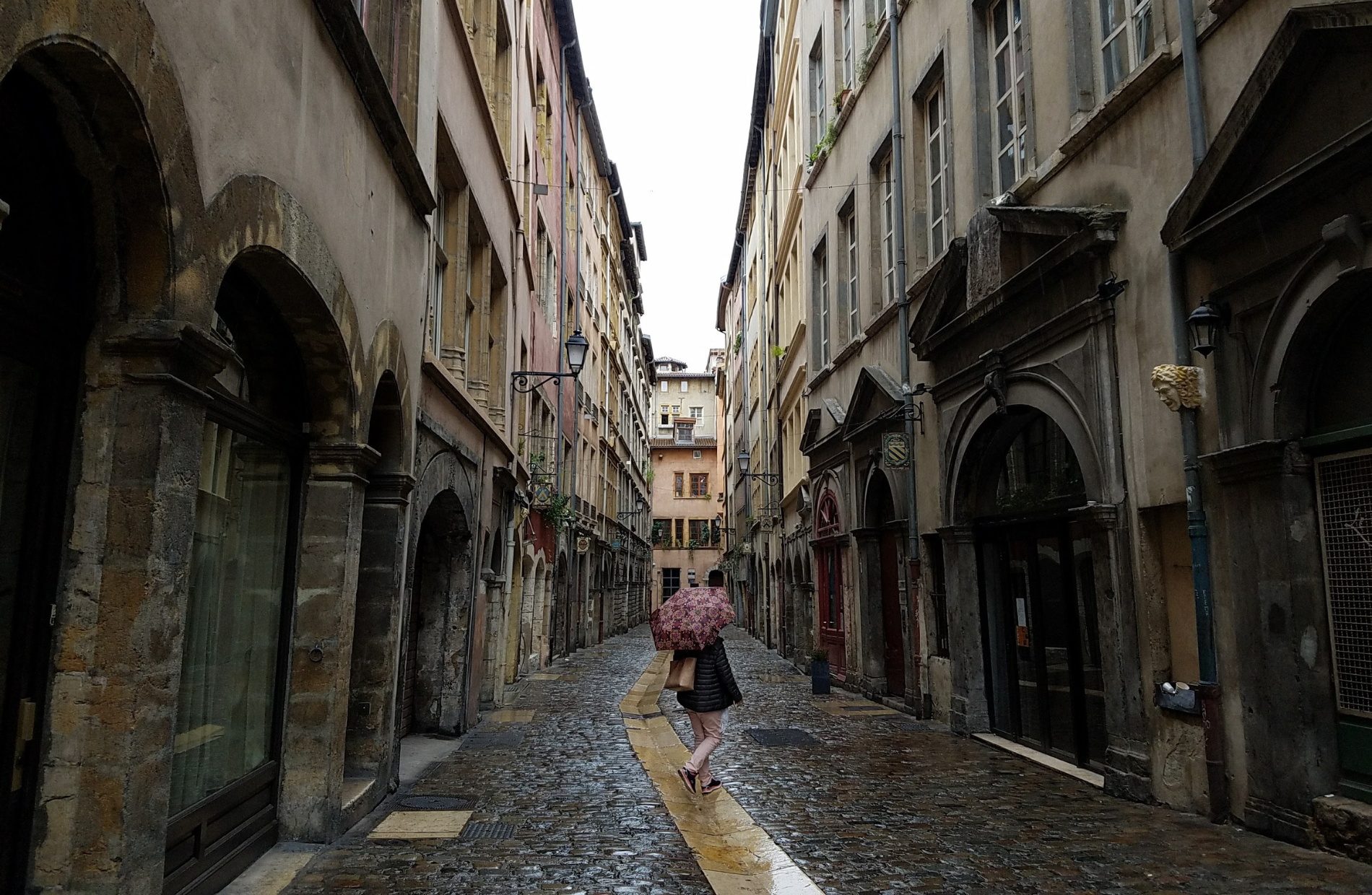 person holding an umbrella walking away on a street lined with gothic style buildings