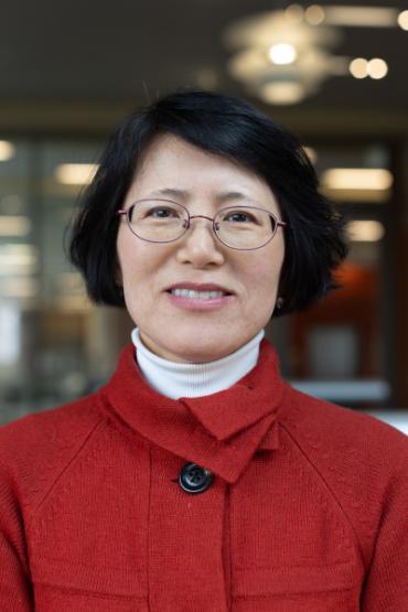 An asian woman wearing glasses and a red coat.