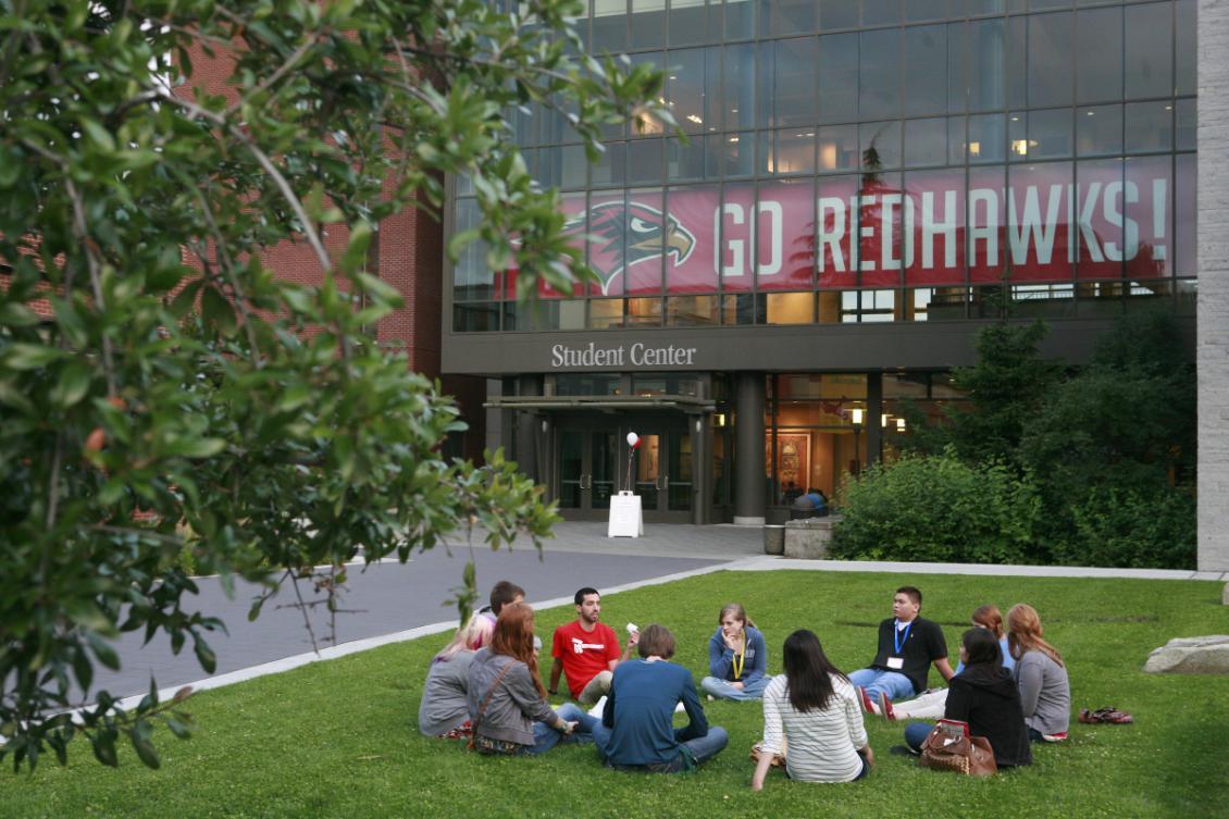 students seated in a circle on lawn outside Student Center