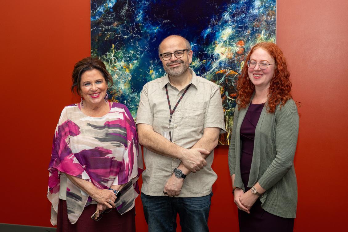 Photography of Rodriguez, Benanti, and Imanaka. The background is a red wall and a painting with blue and green colors.